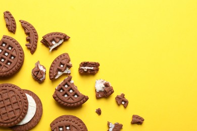Tasty chocolate sandwich cookies with cream on yellow background, flat lay. Space for text