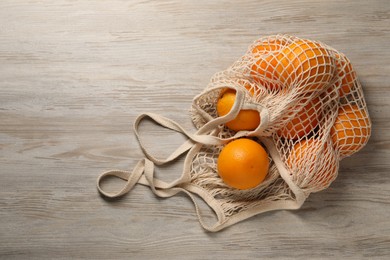 Many ripe juicy oranges with net bag on wooden table, top view. Space for text