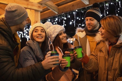 Happy friends with cups of mulled wine at winter fair