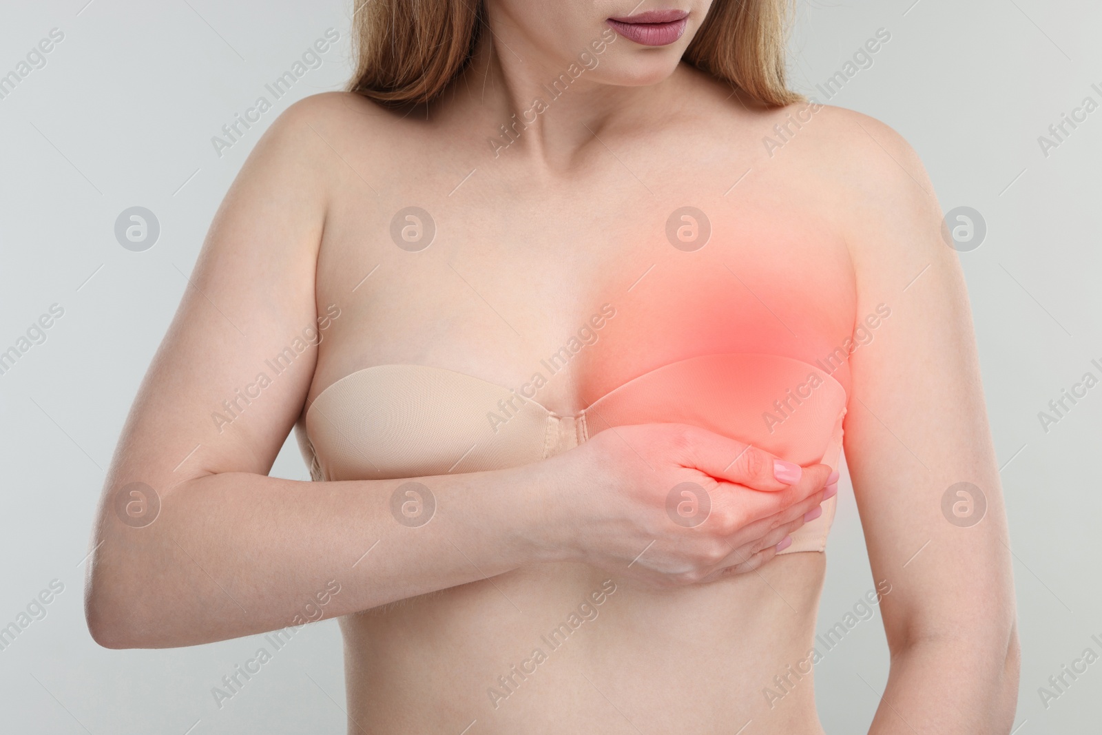 Image of Young woman suffering from breast pain on light background, closeup