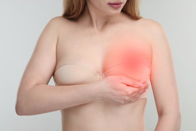 Young woman suffering from breast pain on light background, closeup