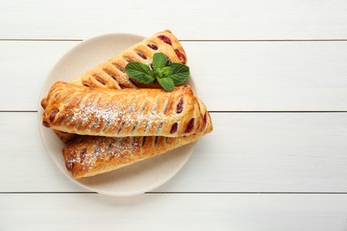 Fresh tasty puff pastry with sugar powder and mint on white wooden table, top view. Space for text