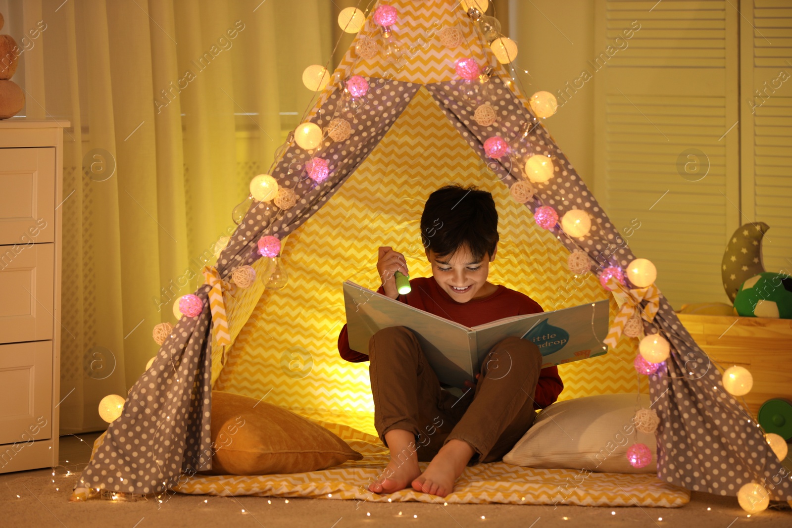 Photo of Boy with flashlight reading book in play tent at home