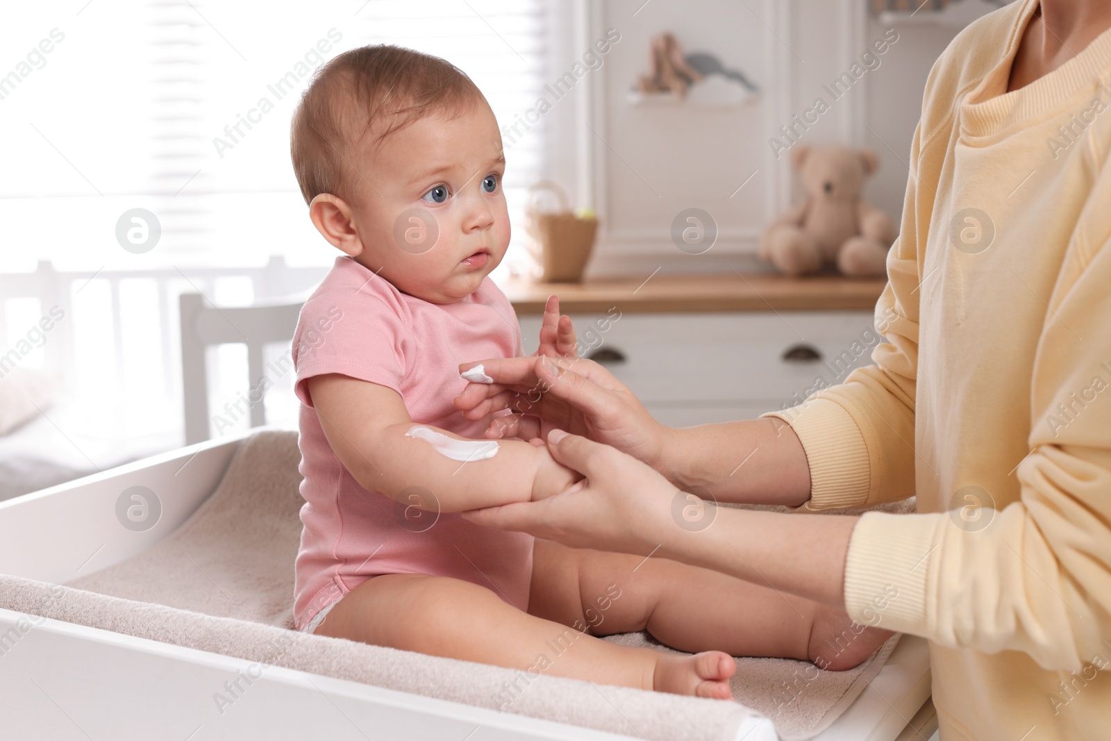 Photo of Mother applying body cream on her little baby at home, closeup