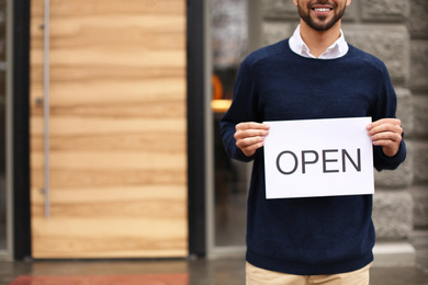 Photo of Young male business owner holding OPEN sign near his cafe, closeup. Space for text