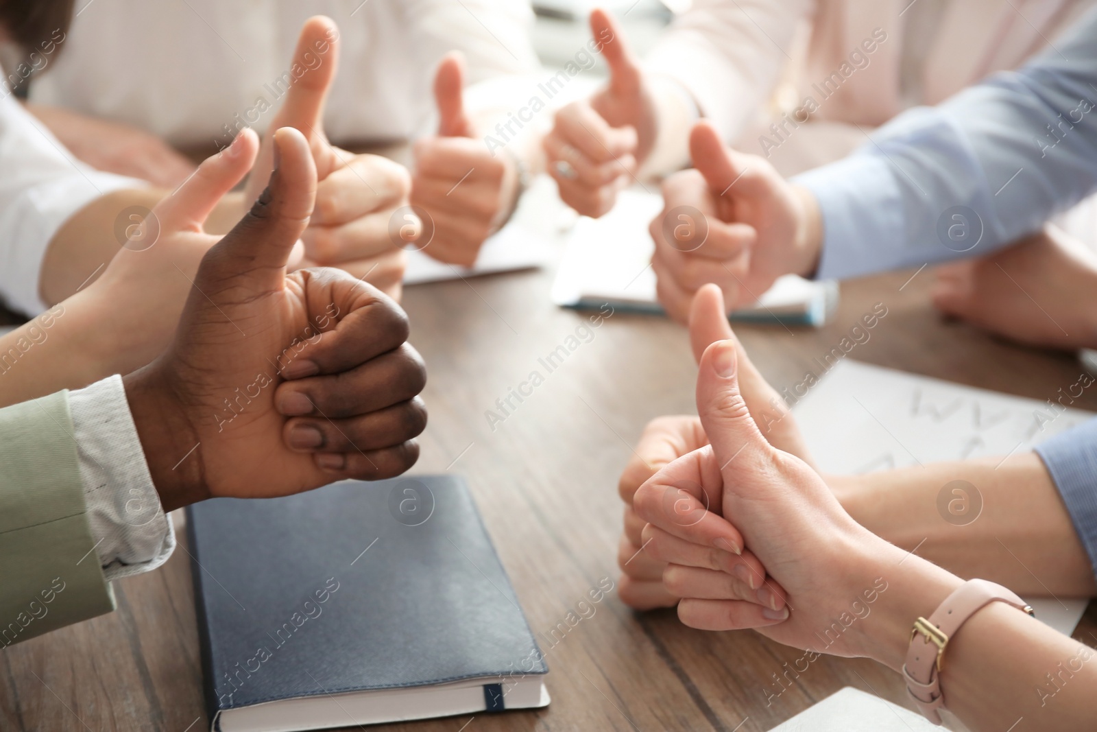 Photo of People showing thumbs up at table, closeup of hands. Unity concept