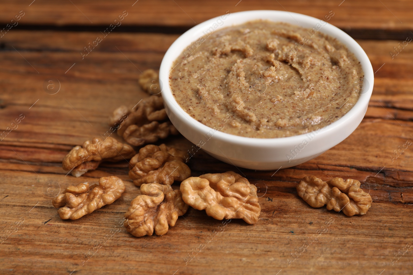 Photo of Delicious nut butter in bowl and walnuts on wooden table, closeup