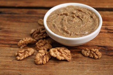 Photo of Delicious nut butter in bowl and walnuts on wooden table, closeup