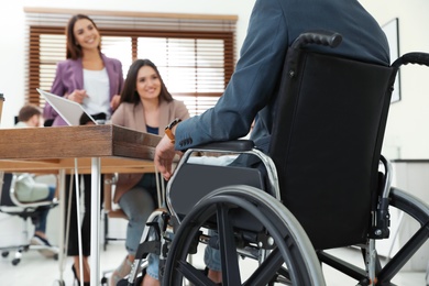 Young man in wheelchair with colleagues at workplace, closeup