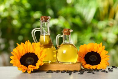 Sunflower cooking oil, seeds and yellow flowers on light grey table outdoors