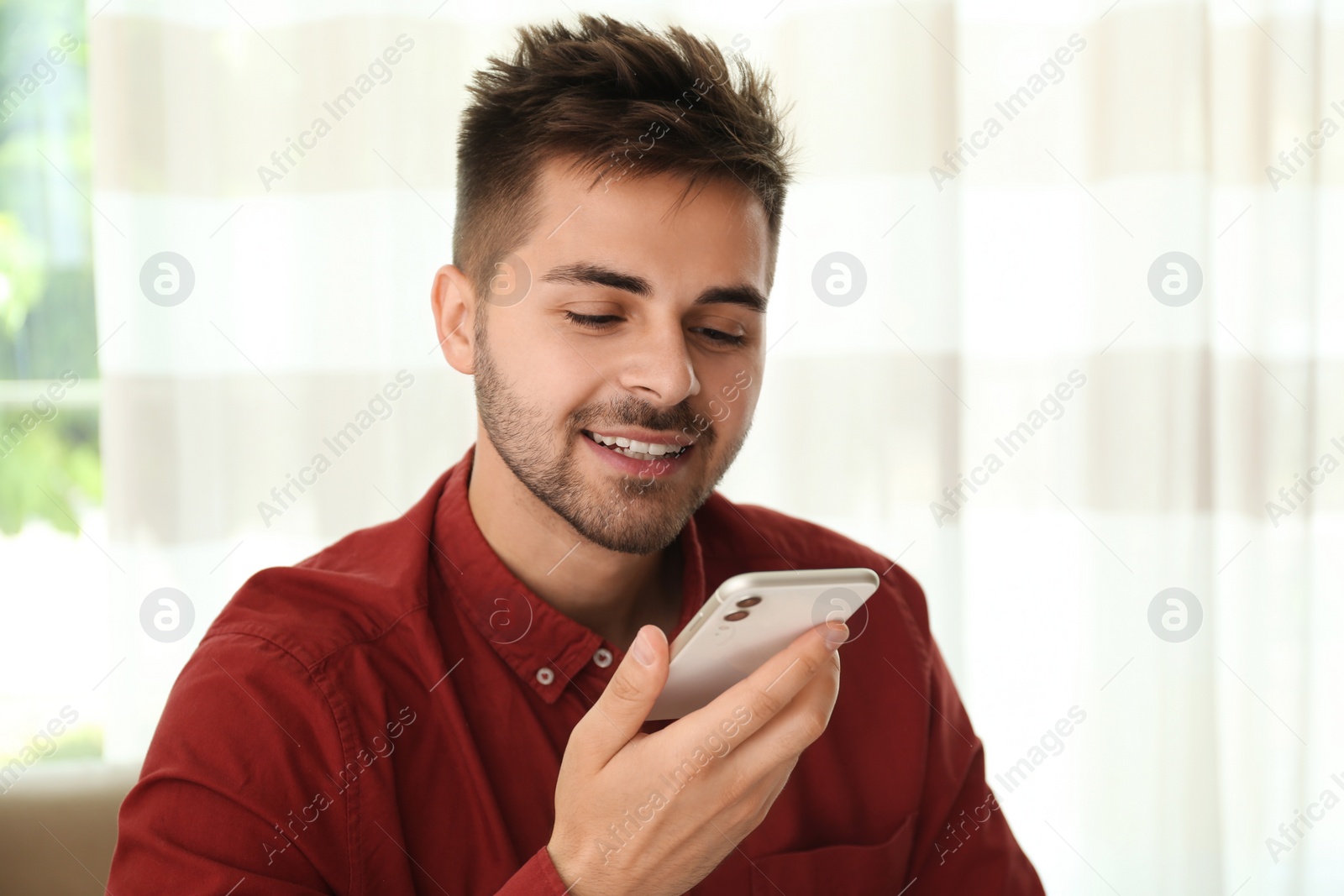 Photo of Young man using voice search on smartphone indoors