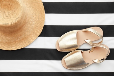 Stylish female shoes and straw hat on striped fabric