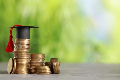 Photo of Scholarship concept. Coins and graduation cap on grey table against blurred background, space for text