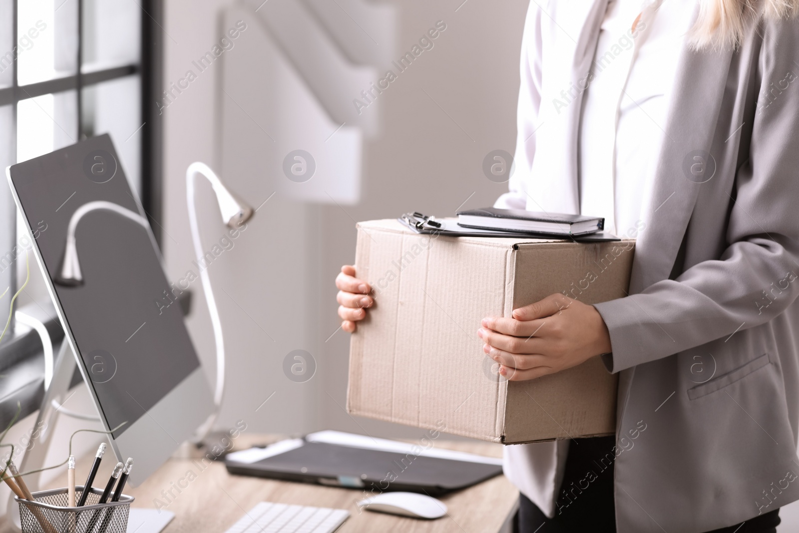 Photo of Young woman holding moving box with office stuff indoors, closeup