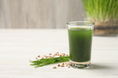 Photo of Wheat grass drink in shot glass, seeds and fresh green sprouts on white wooden table, closeup. Space for text