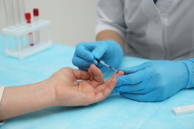 Photo of Doctor taking blood sample from patient's finger at table in clinic, closeup