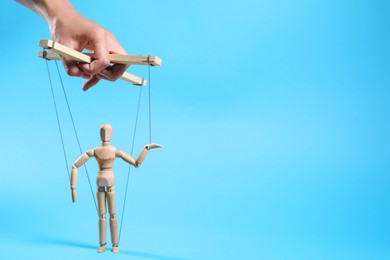 Photo of Man pulling strings of puppet on light blue background, closeup. Space for text