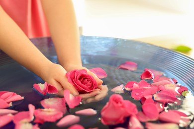 Photo of Child holding rose flower in bowl with water and petals on blurred background, closeup