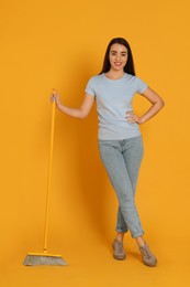 Beautiful young woman with broom on yellow background