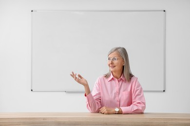 Professor giving lecture at desk in classroom, space for text