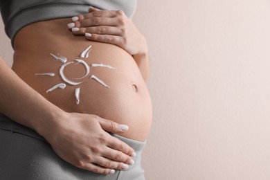 Photo of Pregnant woman with sun protection cream on her belly against beige background, closeup. Space for text