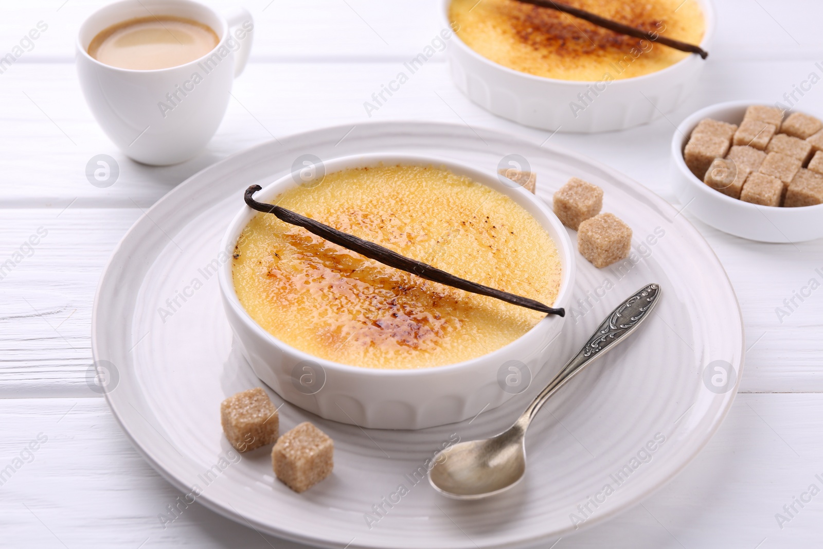Photo of Delicious creme brulee in bowls, vanilla pods, sugar cubes and coffee on white wooden table