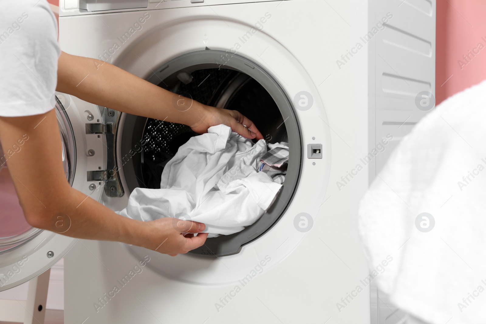 Photo of Woman taking laundry out of washing machine indoors, closeup