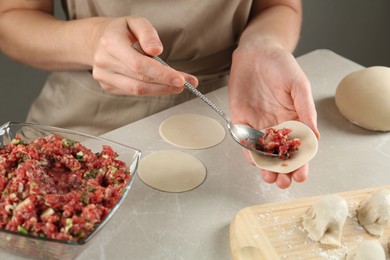 Woman putting gyoza filling in center of dough wrapper at light table, closeup