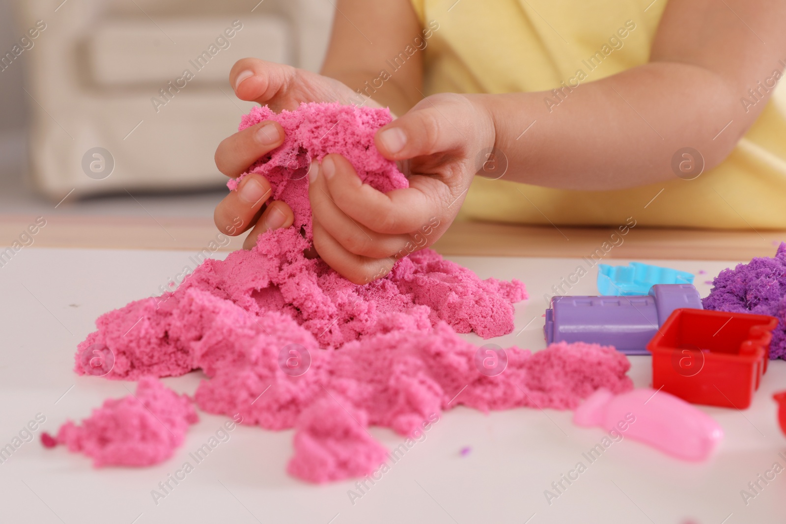 Photo of Little girl playing with bright kinetic sand at table indoors, closeup