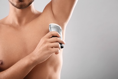 Young man using deodorant on gray background, closeup. Space for text