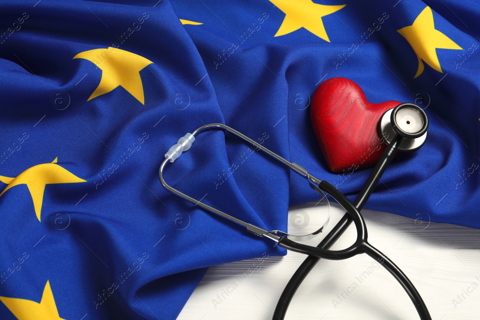 Photo of Stethoscope, red heart and flag of European Union on white wooden table