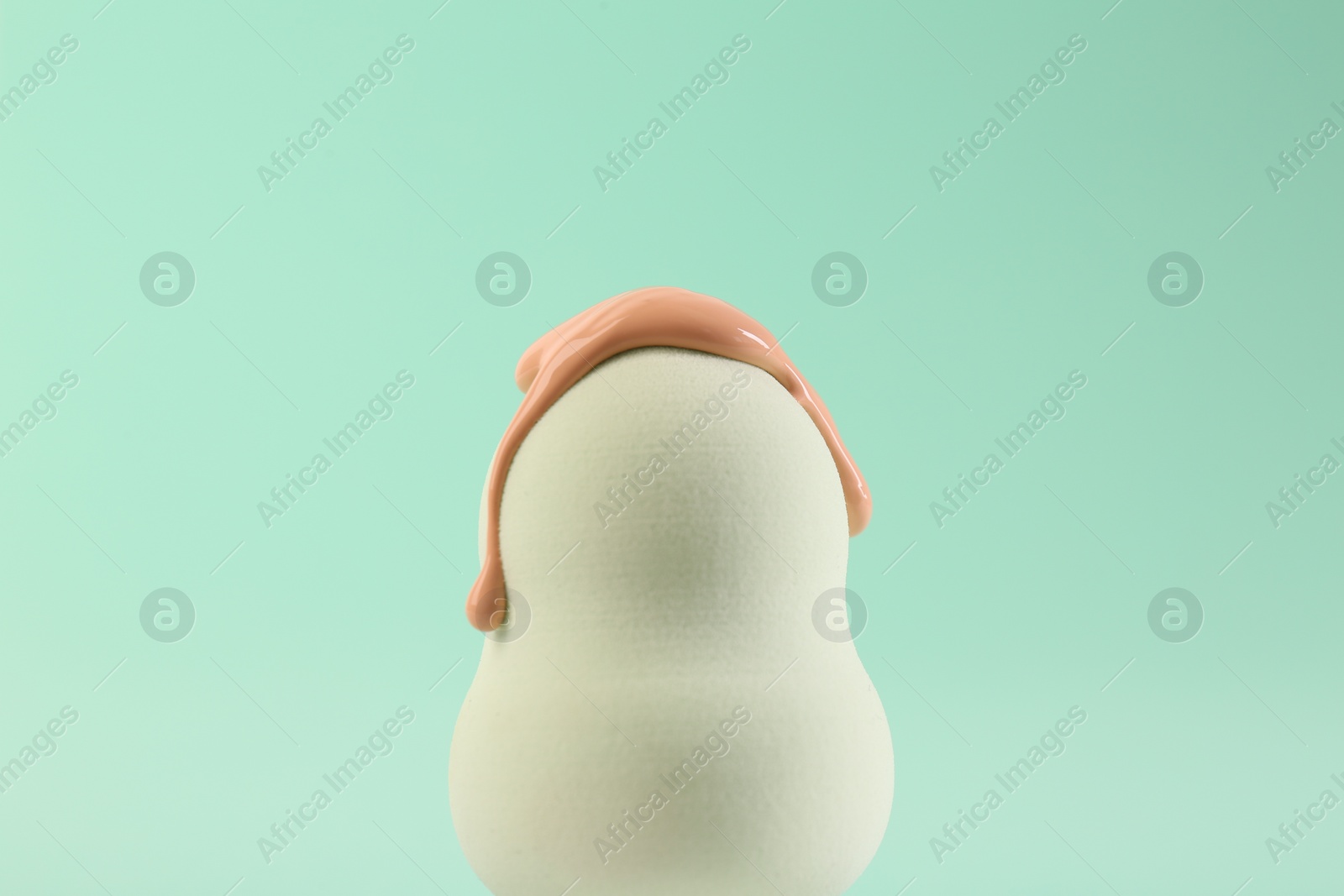 Photo of White makeup sponge with skin foundation on turquoise background, closeup