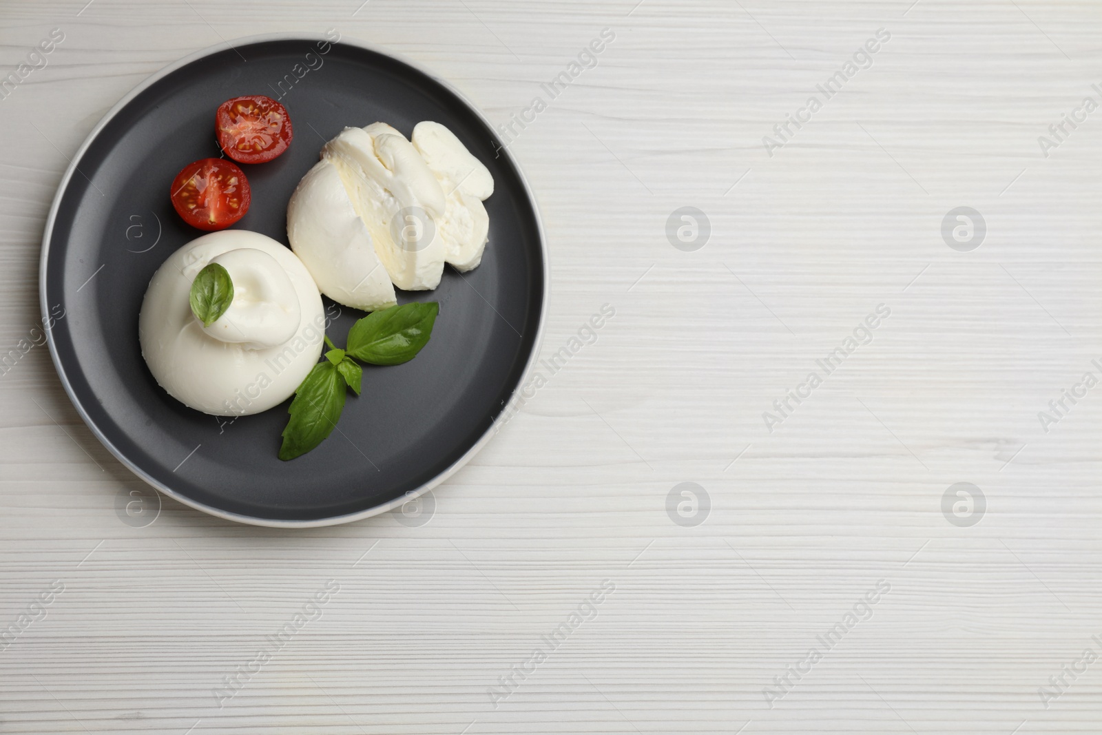 Photo of Delicious burrata cheese with basil and cut tomato on white wooden table, top view. Space for text