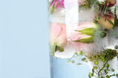 Photo of Glass of water with ice cubes and flowers on color background, closeup. Space for text