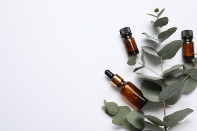 Photo of Aromatherapy. Bottles of essential oil and eucalyptus branches on white background, flat lay. Space for text