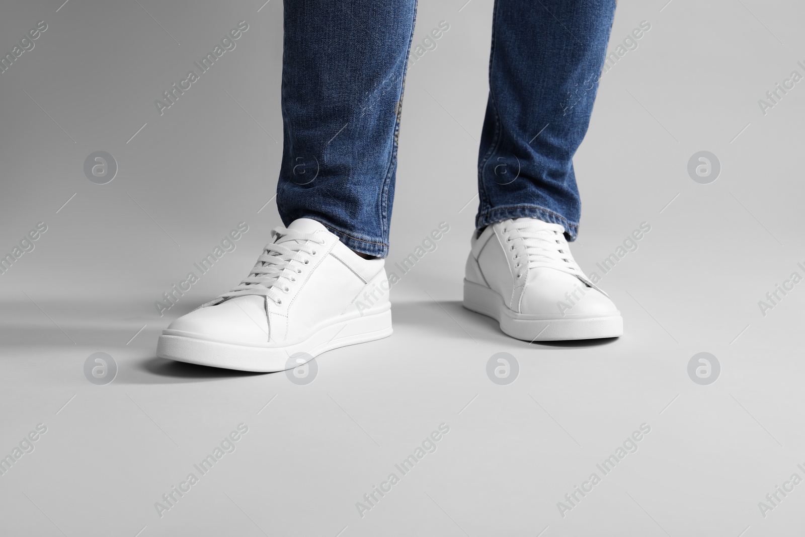 Photo of Man wearing stylish white sneakers on grey background, closeup