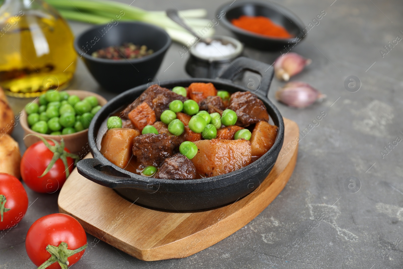 Photo of Delicious beef stew and ingredients on grey table, closeup. Space for text