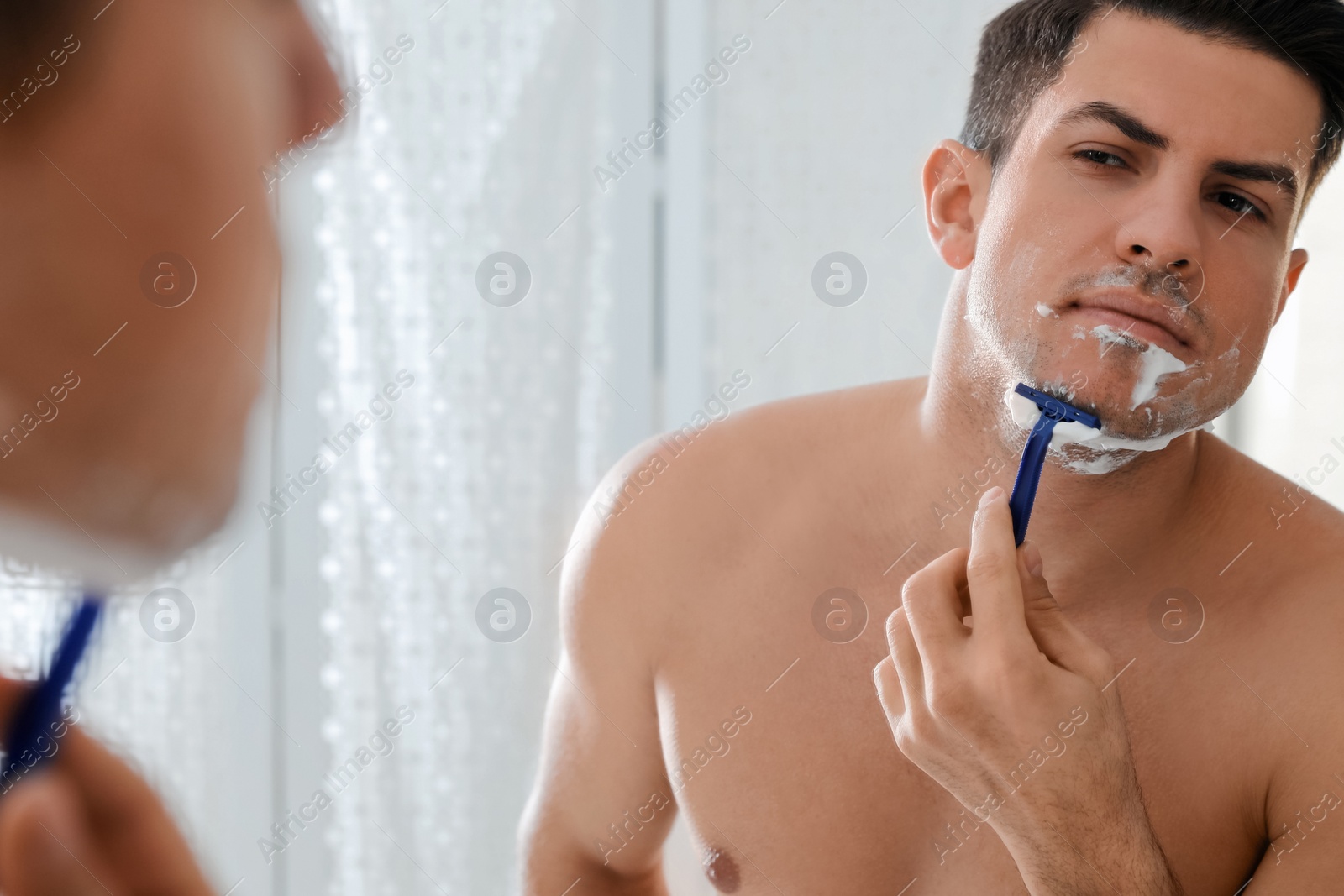 Photo of Handsome man shaving near mirror in bathroom