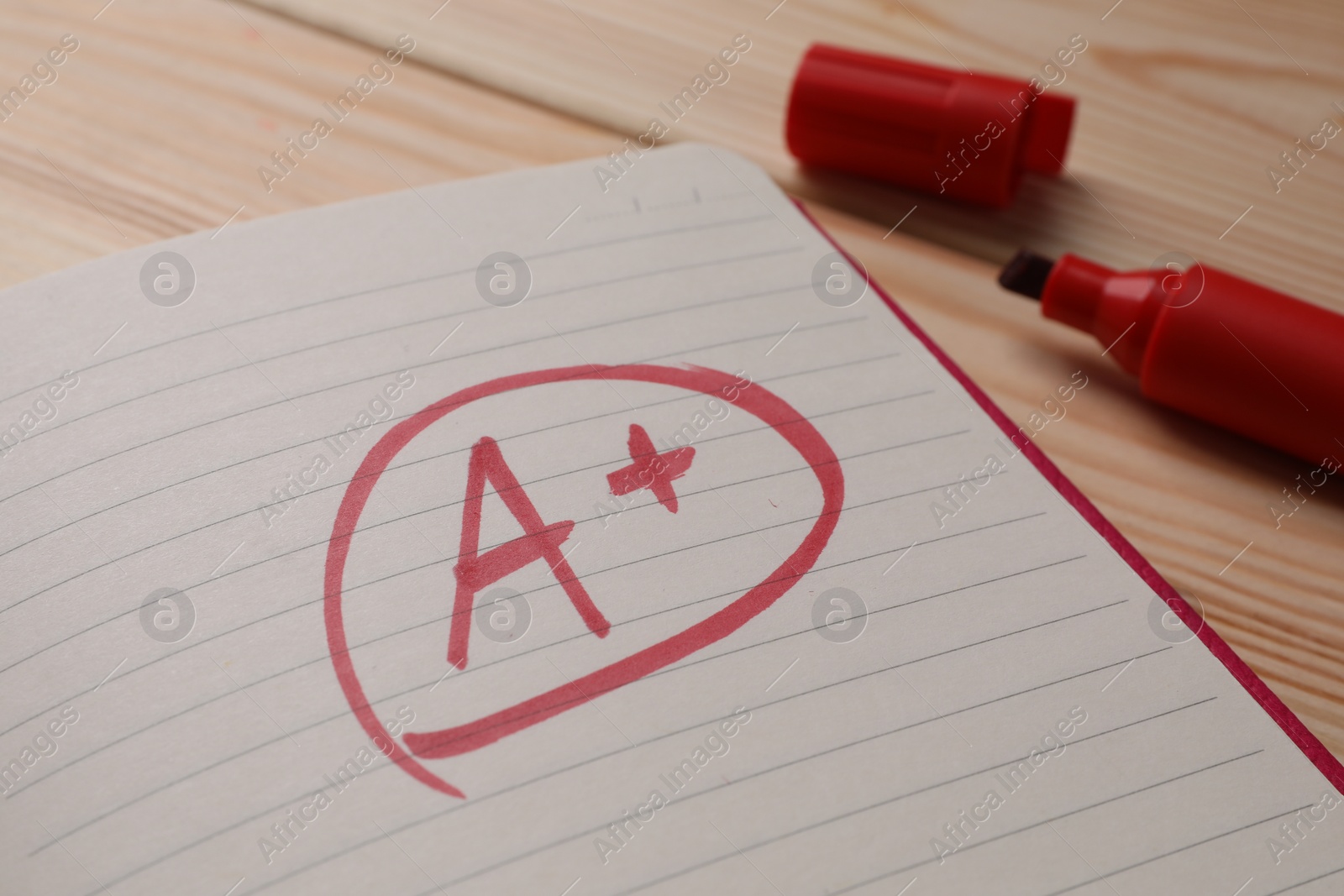 Photo of School grade. Red letter A with plus symbol on notebook paper and marker on table, closeup