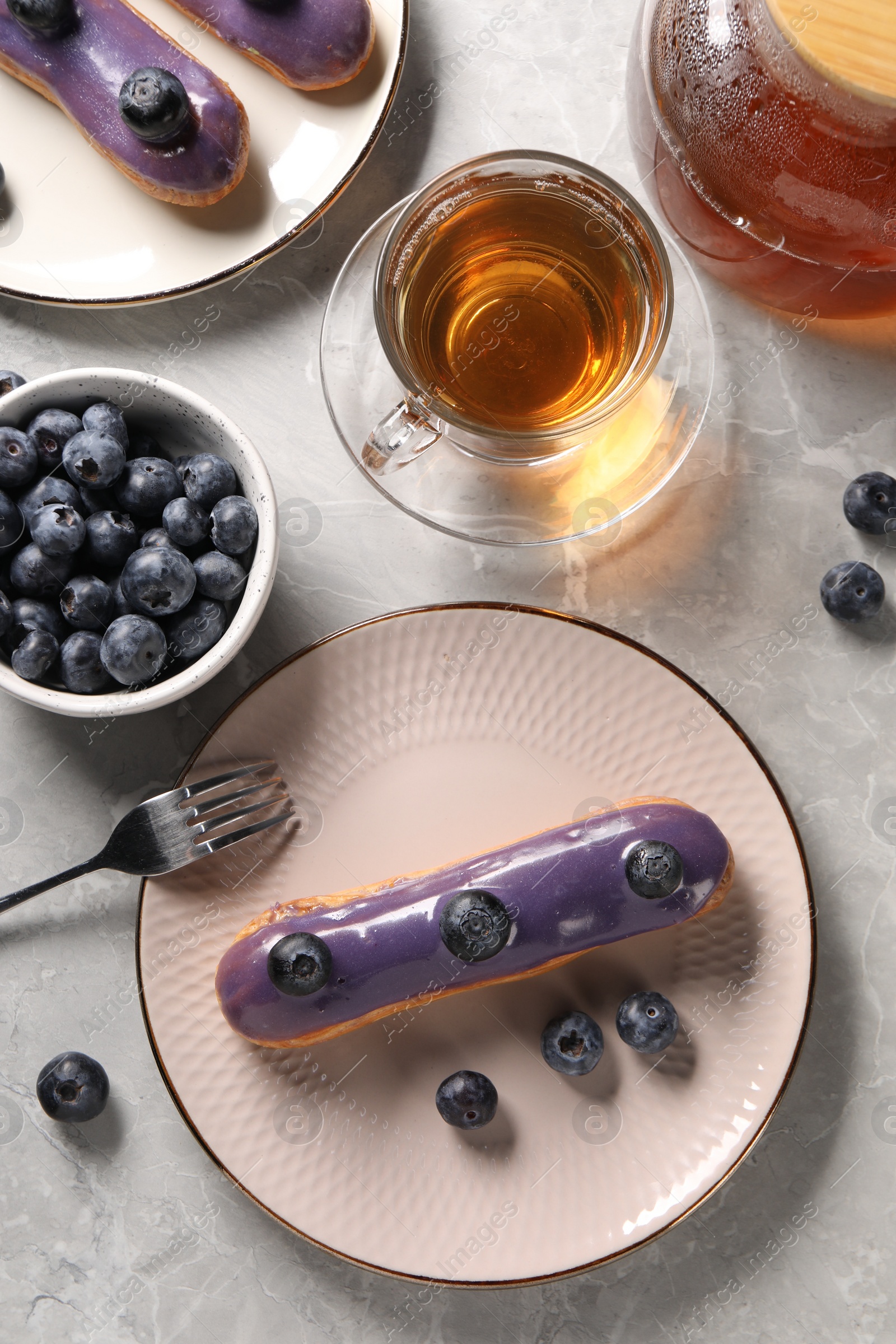 Photo of Tasty glazed eclairs with blueberries and tea on grey marble table, flat lay