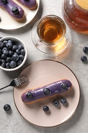 Photo of Tasty glazed eclairs with blueberries and tea on grey marble table, flat lay