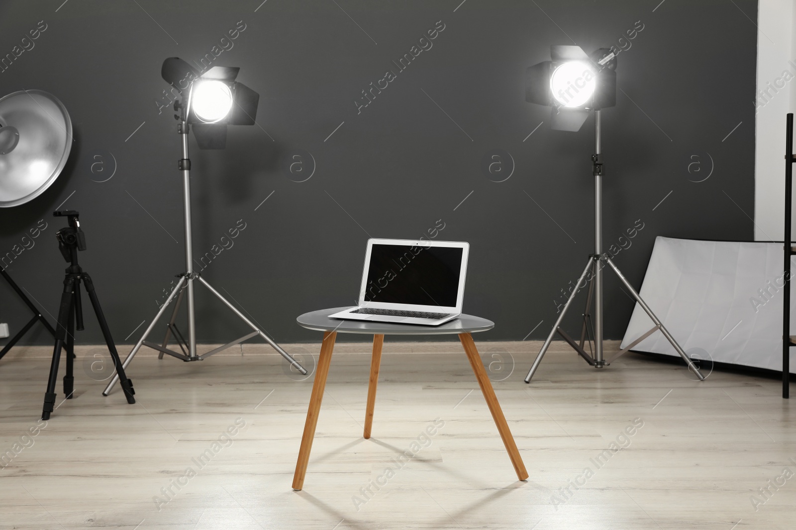 Photo of Interior of modern photo studio with laptop, table and professional equipment