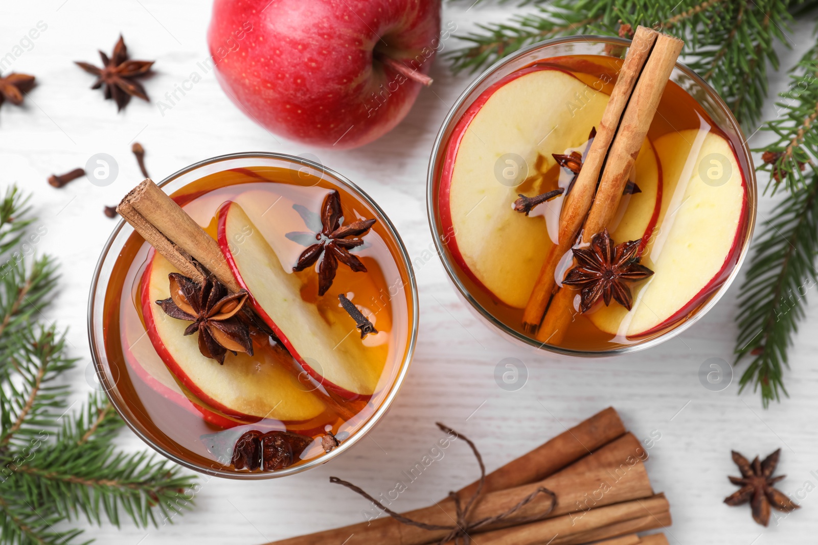 Photo of Hot mulled cider, ingredients and fir branches on white wooden table, flat lay