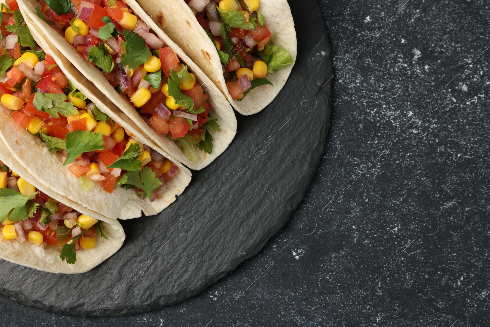 Photo of Tasty tacos with vegetables on black textured table, top view. Space for text