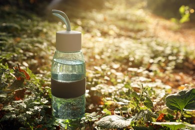 Glass bottle of water in green grass on sunny day. Space for text