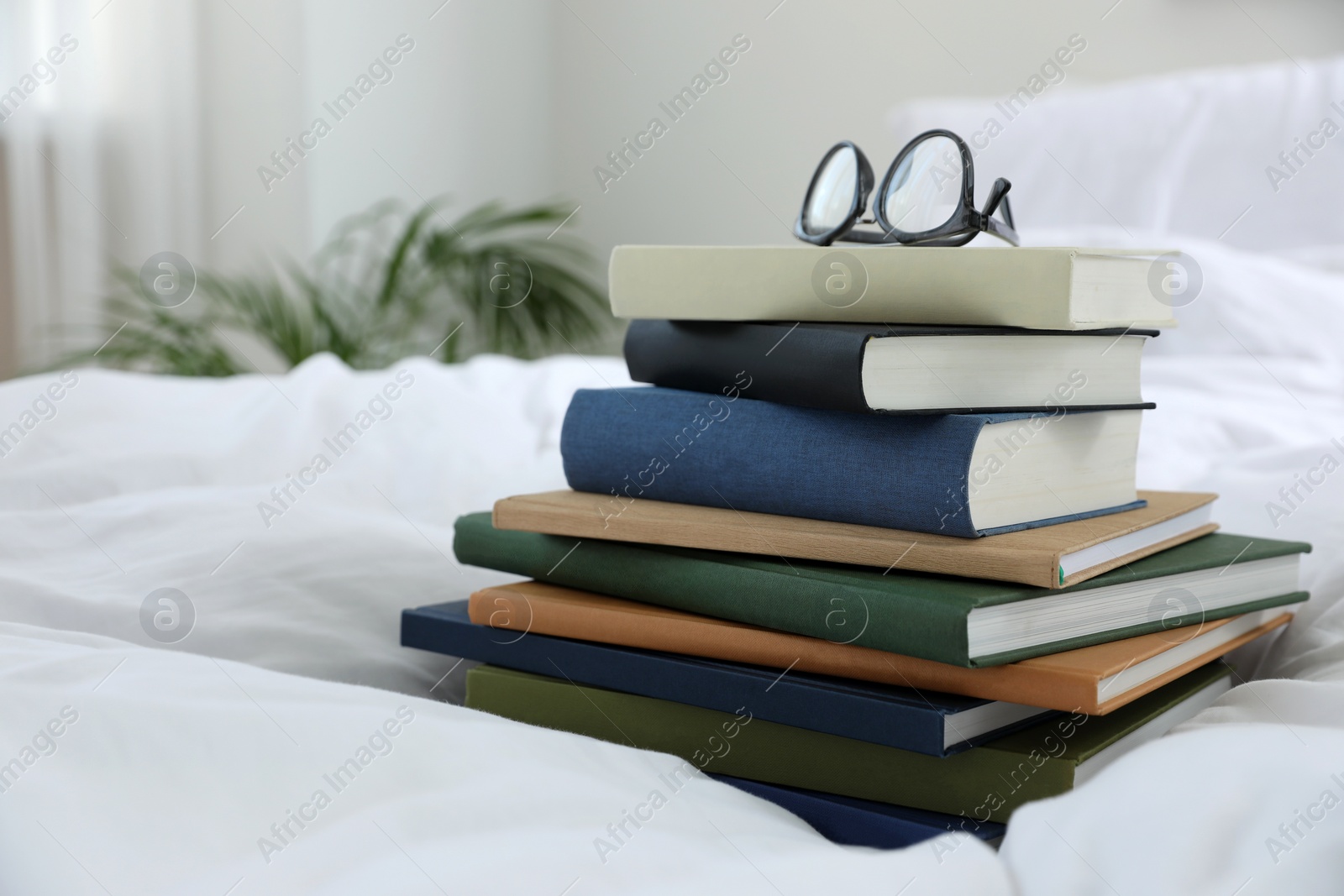 Photo of Hardcover books and glasses on bed indoors