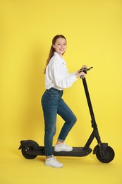 Photo of Happy woman with modern electric kick scooter on yellow background
