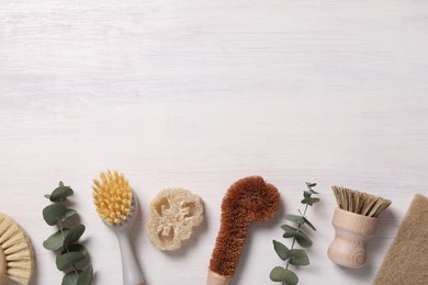 Photo of Cleaning brushes, loofah and eucalyptus leaves on light wooden table, flat lay. Space for text