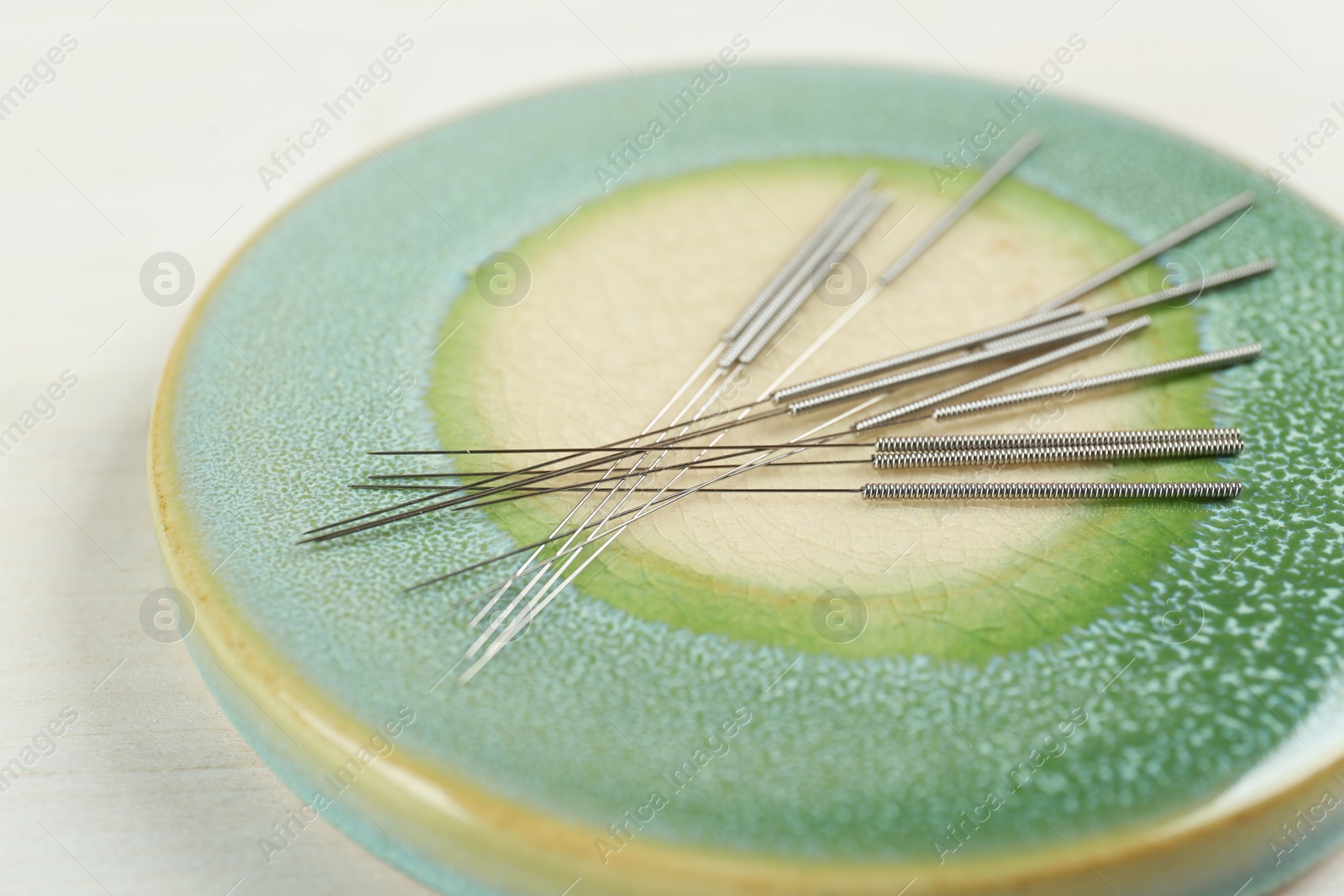 Photo of Light green stone coaster with acupuncture needles on white table, closeup