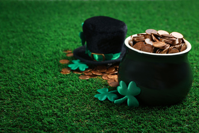 Photo of Pot of gold coins, hat and clover leaves on green grass, space for text. St. Patrick's Day celebration